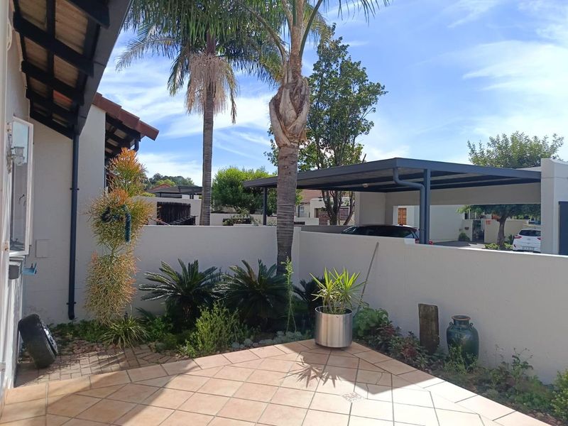 A paved outdoor patio area featuring a boundary wall, established garden landscaping, and a covered carport structure.