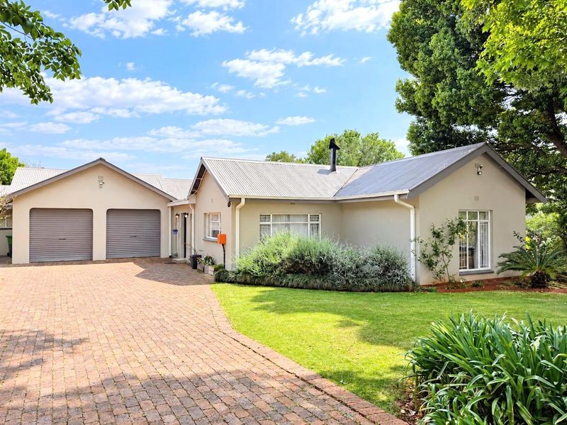 Front view of a well-maintained single-story house featuring a double garage, brick paved driveway, and established garden.