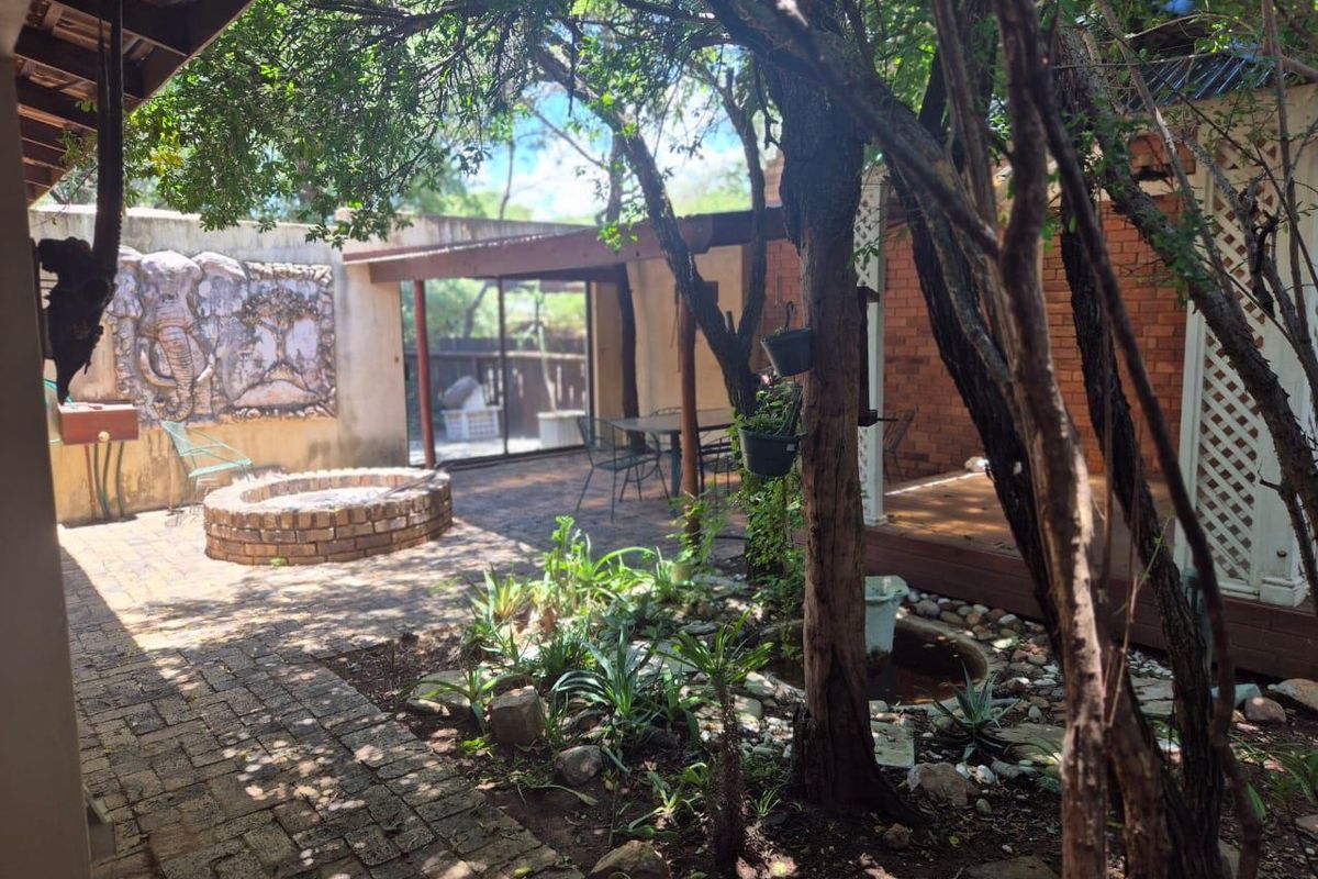 A private outdoor courtyard featuring a brick-paved patio, a built-in fire pit, and a decorative wall mural, offering a secluded garden entertainment space.