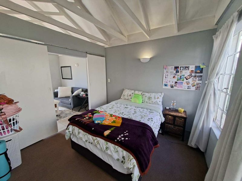 A cozy bedroom featuring exposed timber ceiling beams, sliding doors leading to an adjacent living space, and a classic lattice window.