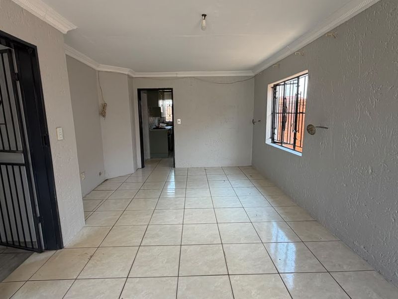 An empty living room featuring tiled flooring, security bars on the window, and a security gate, offering a blank canvas for renovation.