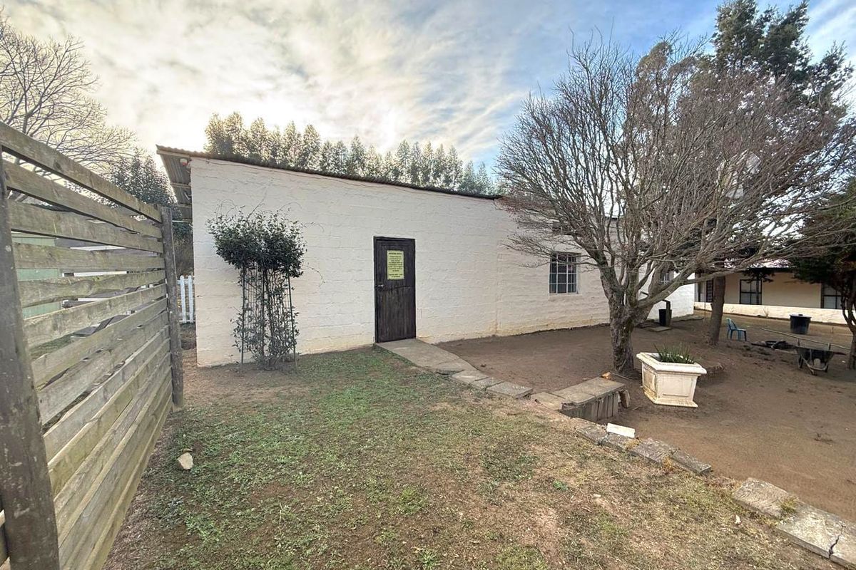 Rear exterior view of a small holding building featuring a white masonry wall, timber door, and stone pathway leading through the garden area.