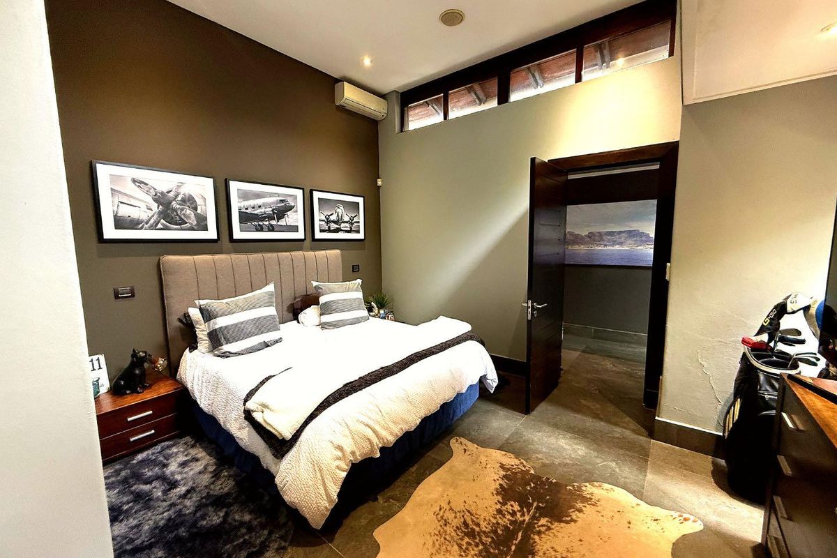 A well-maintained bedroom featuring high ceilings with clerestory windows, tiled flooring, and a wall-mounted air conditioning unit.