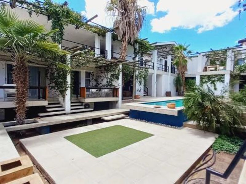 Rear exterior view featuring a swimming pool, tiled patio area, multi-level balconies, and pergola structures with established climbing vegetation.