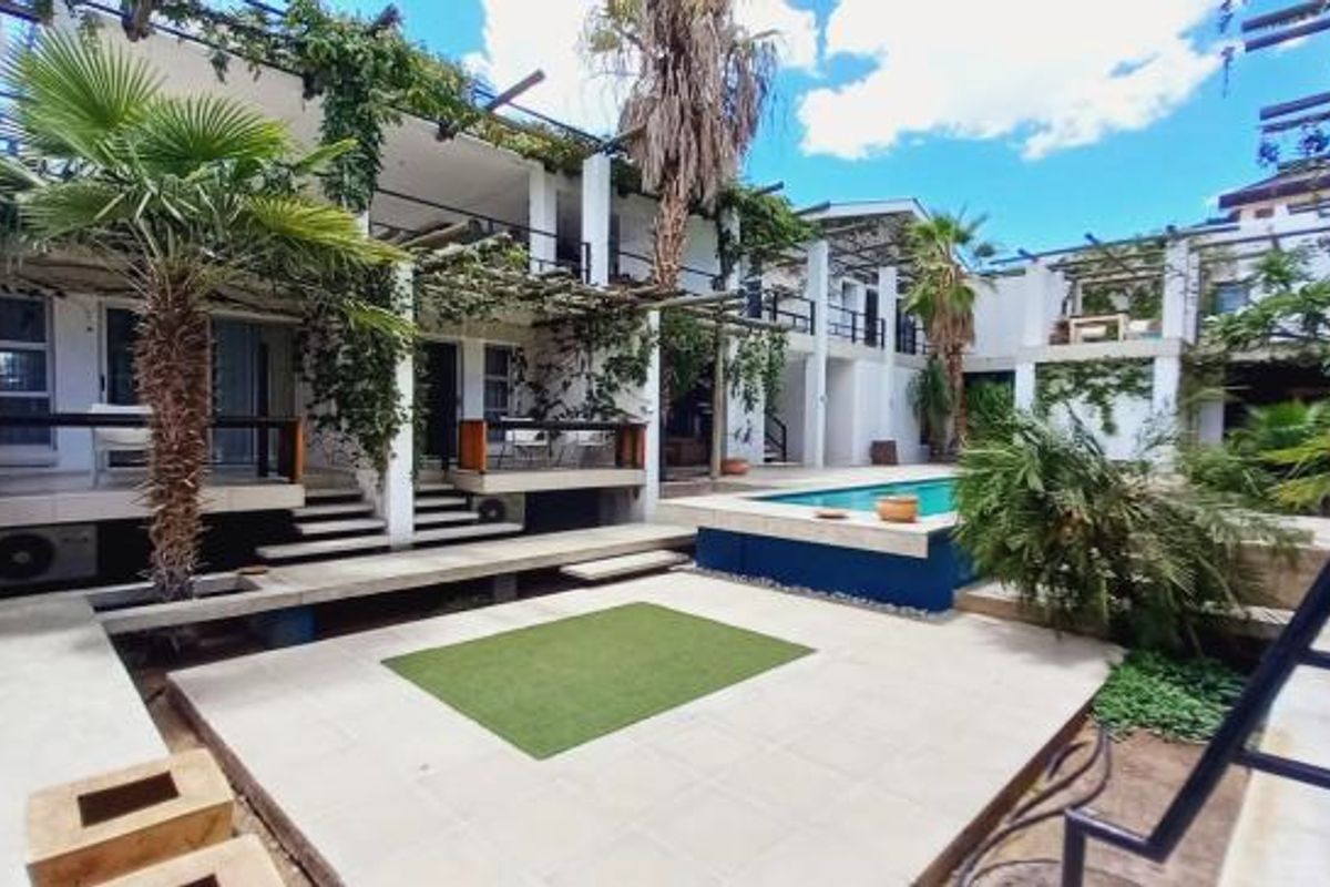 Rear exterior view featuring a swimming pool, tiled patio area, multi-level balconies, and pergola structures with established climbing vegetation.