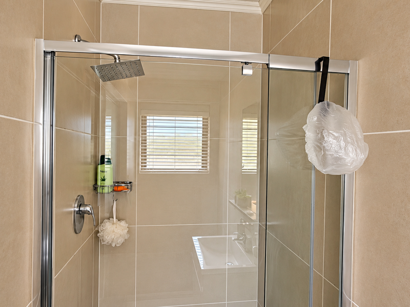 A modern shower enclosure featuring a rainfall shower head, chrome mixer, and neutral wall tiling with a window for natural light.