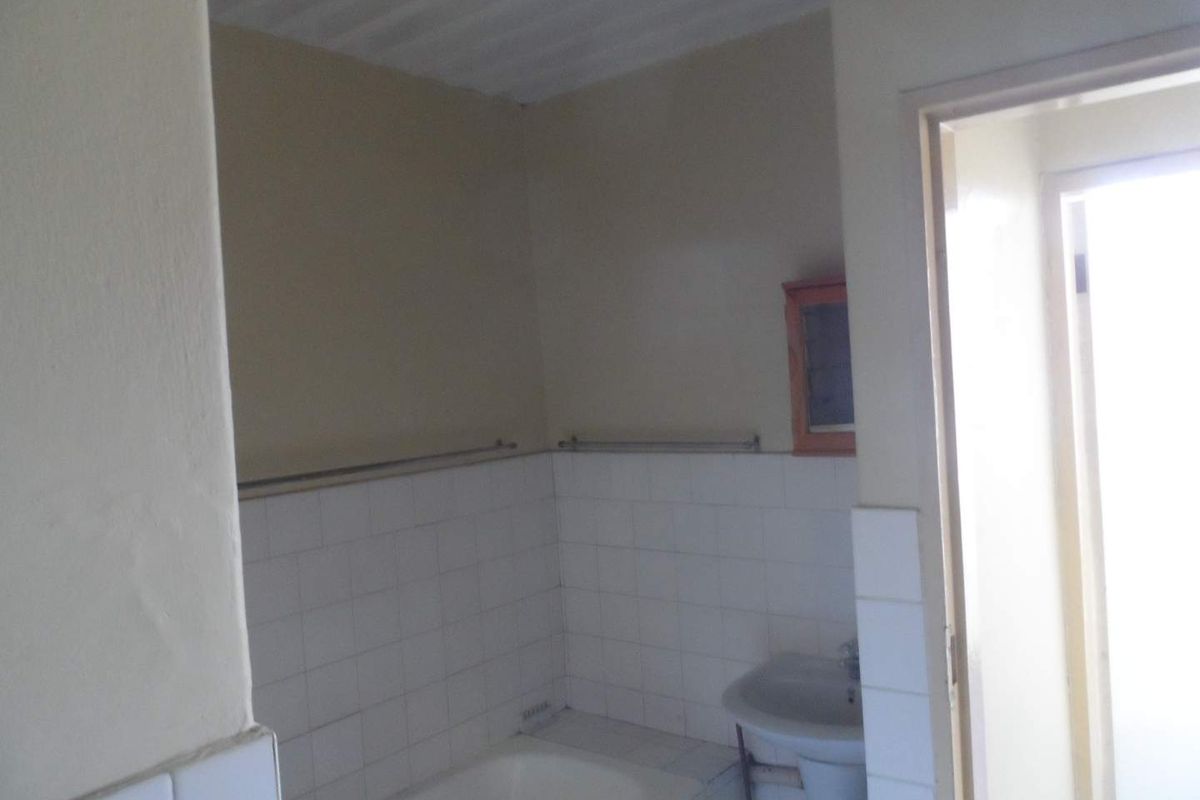 A functional bathroom featuring a built-in bathtub, pedestal sink, and tiled splashbacks, offering a basic layout ready for potential modernization.