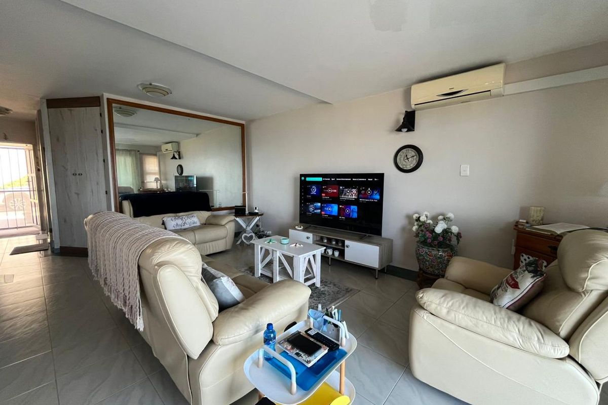 A living room featuring tiled flooring, a large wall mirror, and a wall-mounted split-system air conditioner.
