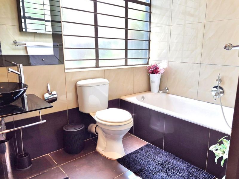 A compact bathroom featuring a built-in bathtub, a modern vessel sink with a glass vanity, and tiled walls and flooring.