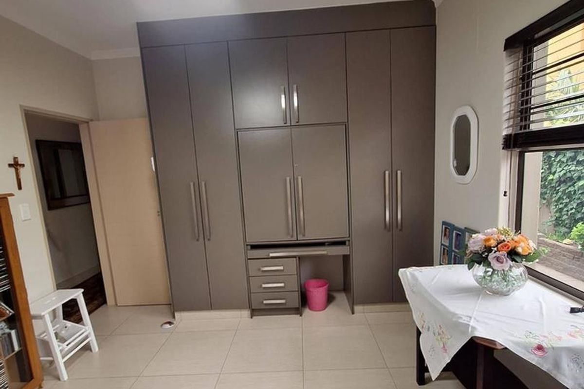 A well-maintained bedroom featuring extensive built-in cabinetry, neutral tiled flooring, and a modern ceiling fan, offering ample storage and a clean aesthetic.
