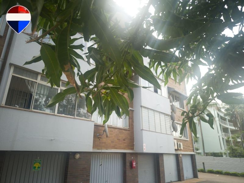 Exterior view of an apartment building featuring a brick and painted facade with multiple ground-level garage doors and security-fitted windows.