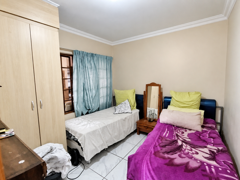 A functional bedroom featuring tiled flooring, a built-in wardrobe, and decorative cornice detailing, providing a practical space for rest.