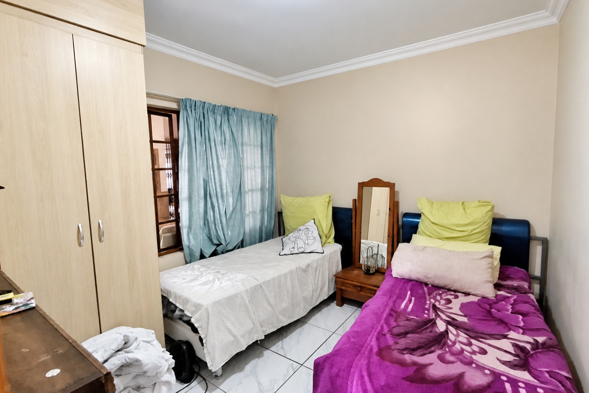 A functional bedroom featuring tiled flooring, a built-in wardrobe, and decorative cornice detailing, providing a practical space for rest.