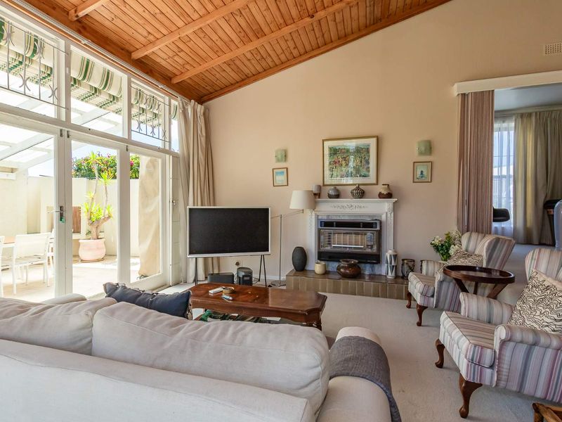 Spacious living room featuring a vaulted timber ceiling, a traditional fireplace with a tiled hearth, and large glass doors opening to an outdoor patio area.