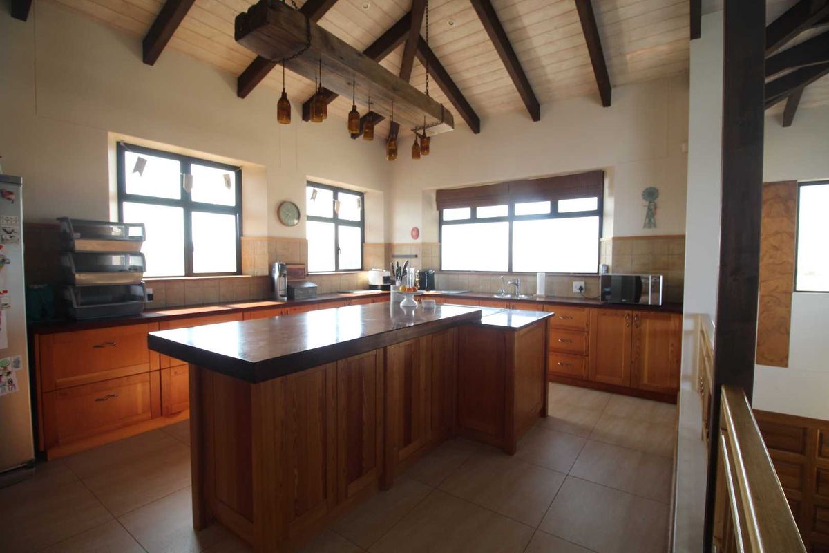 Spacious kitchen featuring warm wooden cabinetry, a central island, vaulted ceilings with exposed timber beams, and ample natural light from multiple windows.