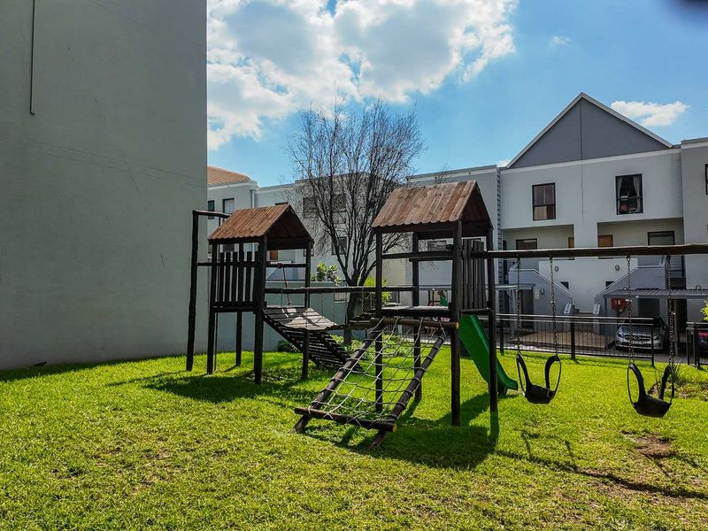 A communal outdoor area featuring a wooden playground structure set on a grass lawn within an apartment complex.