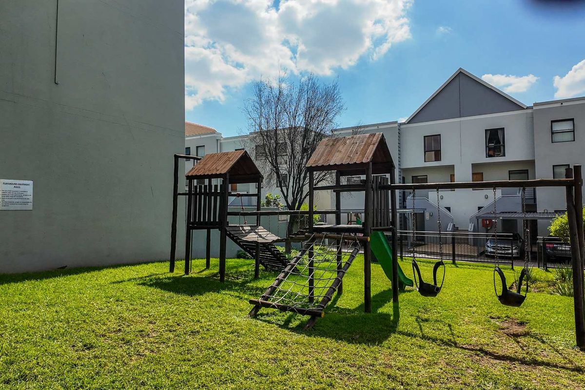 A communal outdoor area featuring a wooden playground structure set on a grass lawn within an apartment complex.