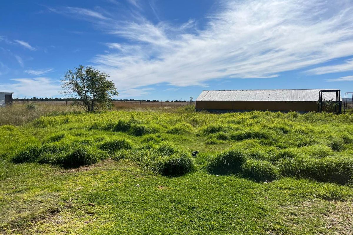 Expansive open farm land featuring a corrugated metal outbuilding and natural grass landscape under a clear blue sky.