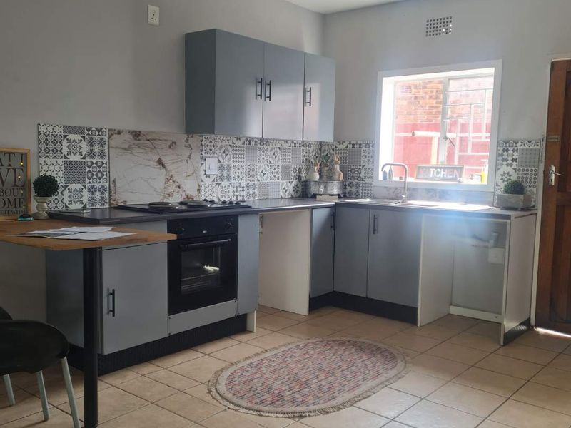 A functional kitchen featuring grey cabinetry, a built-in oven and hob, patterned tiled backsplash, and tiled flooring with a window for natural light.