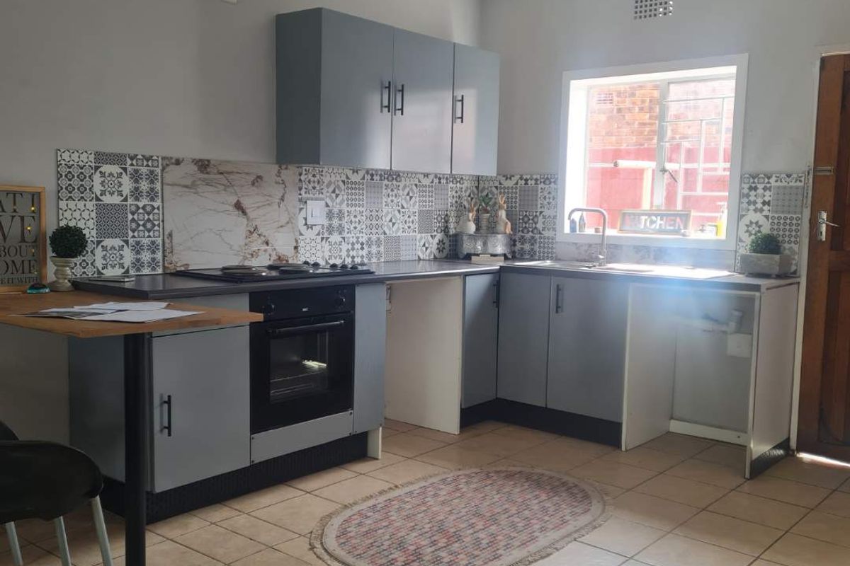 A functional kitchen featuring grey cabinetry, a built-in oven and hob, patterned tiled backsplash, and tiled flooring with a window for natural light.