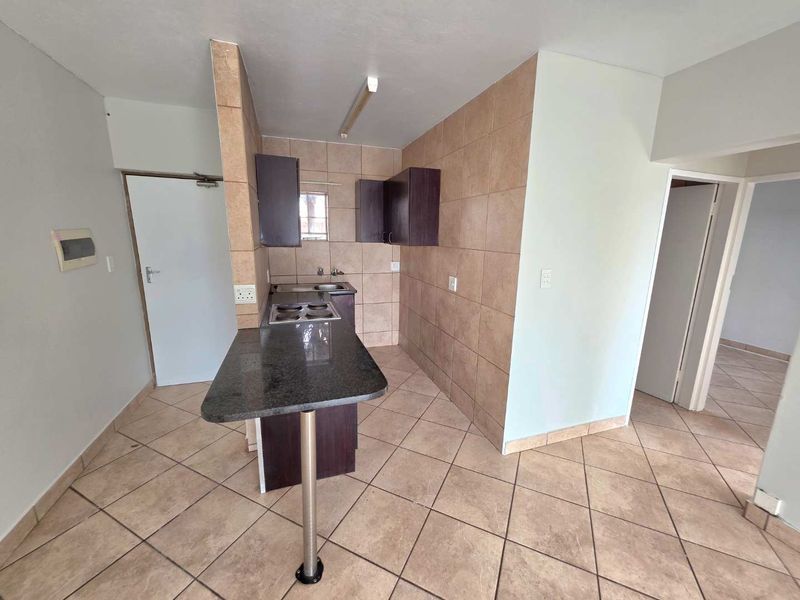 A compact kitchen featuring a granite breakfast bar, built-in cabinetry, and ceramic tiling throughout, offering a functional layout in an open-plan apartment setting.