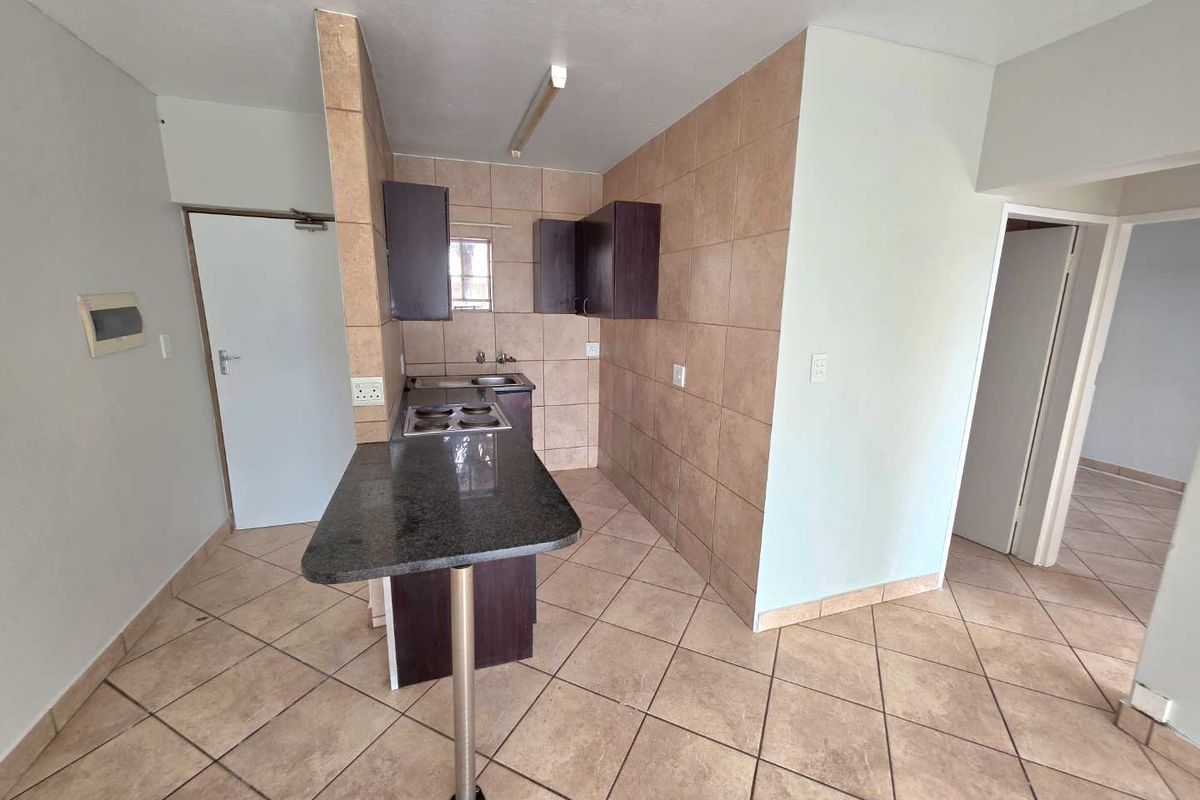 A compact kitchen featuring a granite breakfast bar, built-in cabinetry, and ceramic tiling throughout, offering a functional layout in an open-plan apartment setting.