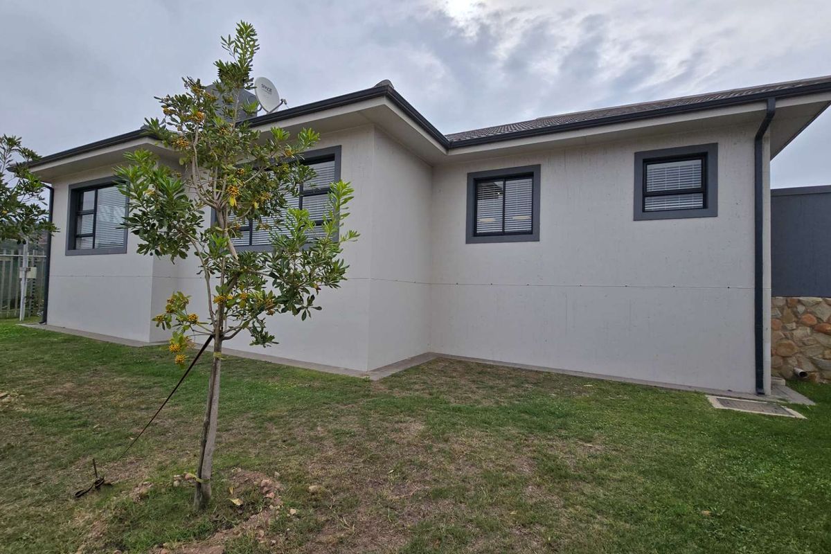 A view of the rear exterior of the retirement unit, featuring modern rendered walls, dark window frames, and a small landscaped garden area.