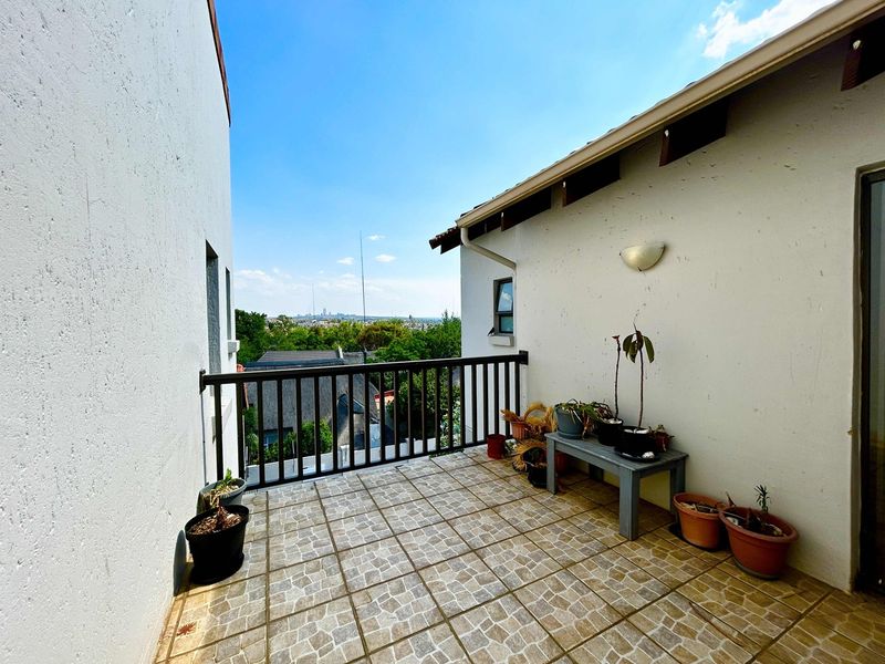 An open-air balcony featuring tiled flooring and a metal balustrade, offering elevated views of the surrounding neighborhood.
