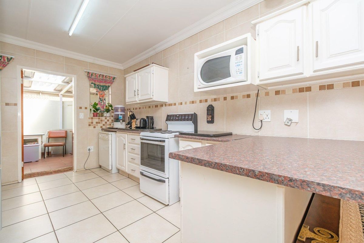 A functional kitchen featuring white cabinetry, laminate countertops, tiled backsplash, and tiled flooring, with a direct view into an adjacent utility area.