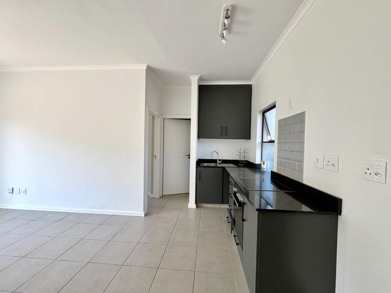 Modern kitchen featuring dark cabinetry, granite countertops, built-in oven, and subway tile backsplash, set within an open-plan living area with tiled flooring.