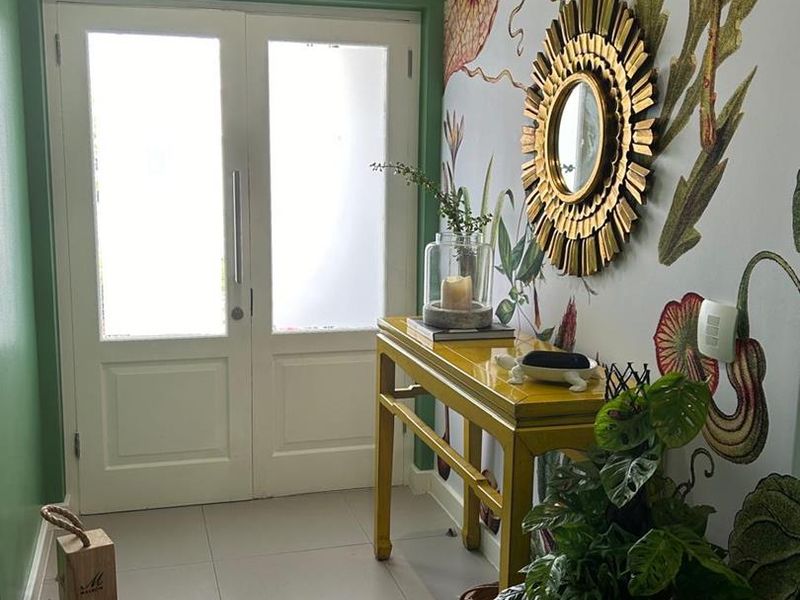 A bright and welcoming entrance hall featuring double doors, large format floor tiles, and a striking floral feature wall.