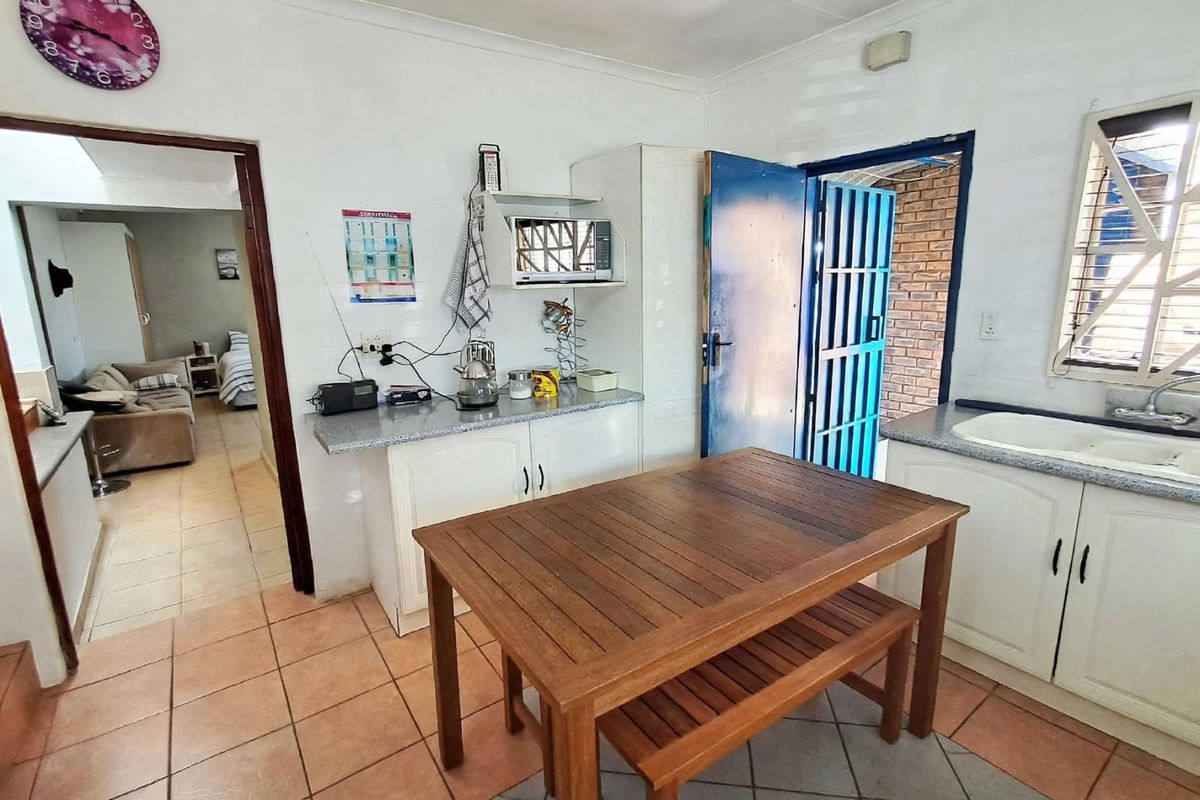 Functional kitchen area featuring built-in cabinetry, laminate countertops, double basin sink, and direct access to an exterior security gate.