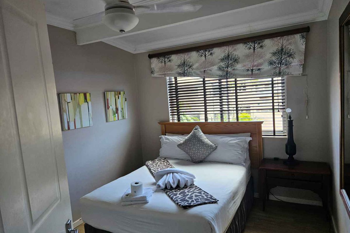 A cozy bedroom featuring a ceiling fan, crown molding, and a window with fitted blinds, providing a comfortable and functional sleeping space.