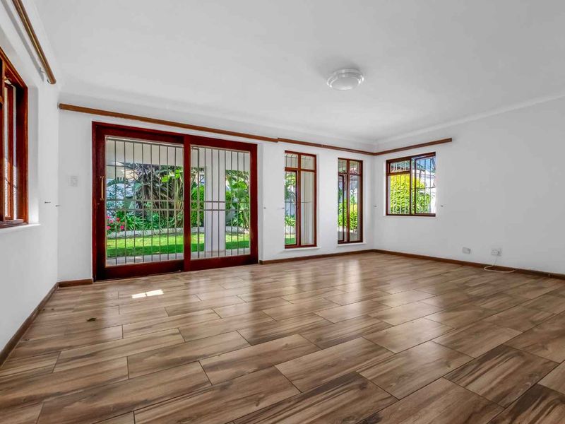 Spacious, sunlit living area featuring wood-look tile flooring, large sliding glass doors with security gates, and views of the garden.