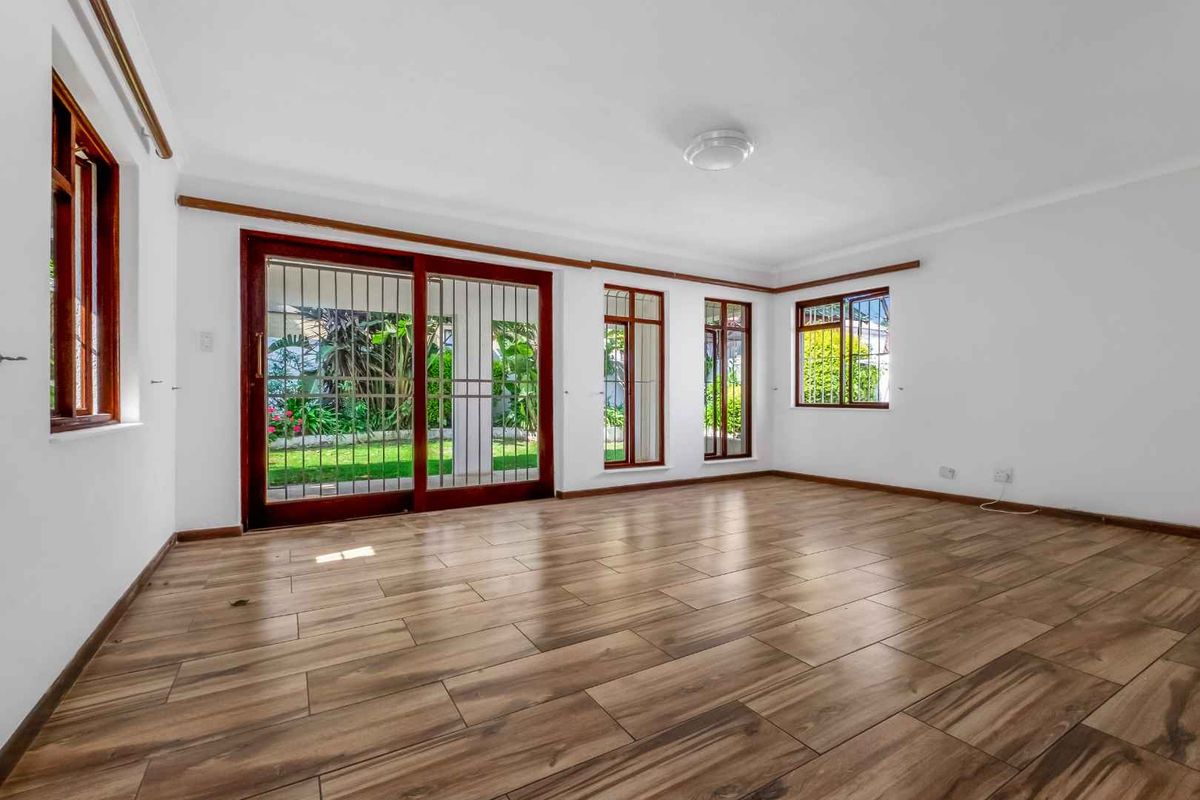Spacious, sunlit living area featuring wood-look tile flooring, large sliding glass doors with security gates, and views of the garden.