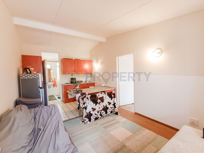 Open plan living and kitchen area featuring tiled flooring, functional cabinetry, and wall-mounted lighting in a retirement village setting.