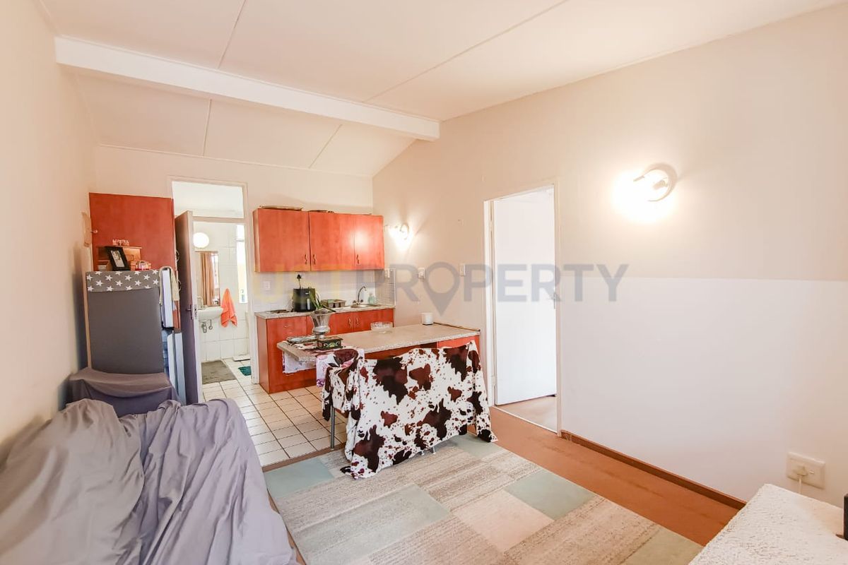 Open plan living and kitchen area featuring tiled flooring, functional cabinetry, and wall-mounted lighting in a retirement village setting.