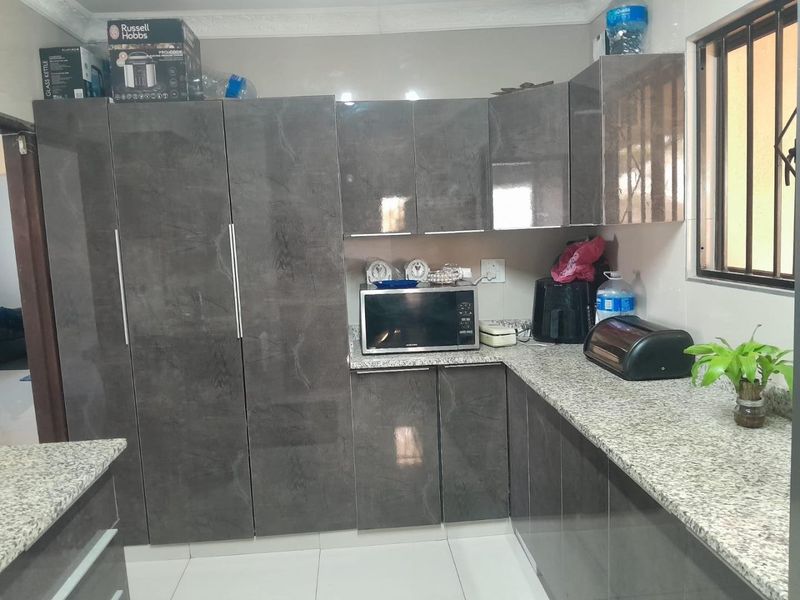 Modern kitchen featuring high-gloss grey cabinetry, granite countertops, and tiled flooring, offering a clean and functional workspace.