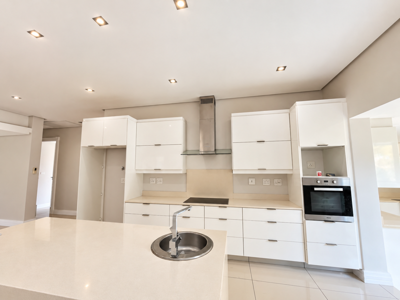 Modern kitchen featuring sleek white cabinetry, stone countertops, a central island with sink, and integrated appliances including an oven and extractor fan.