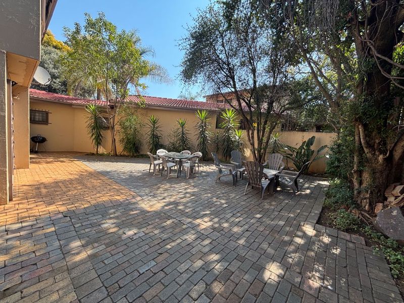 A spacious rear paved patio area featuring established trees, boundary walls, and a tiled roof section of the townhouse.