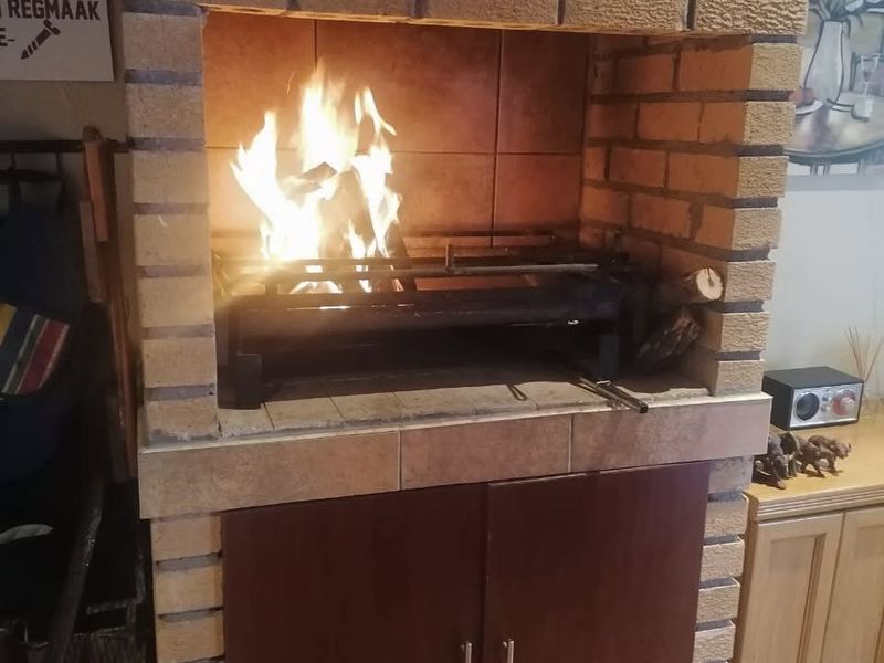 A traditional indoor brick fireplace and built-in braai area featuring a tiled hearth and integrated lower storage cabinetry.