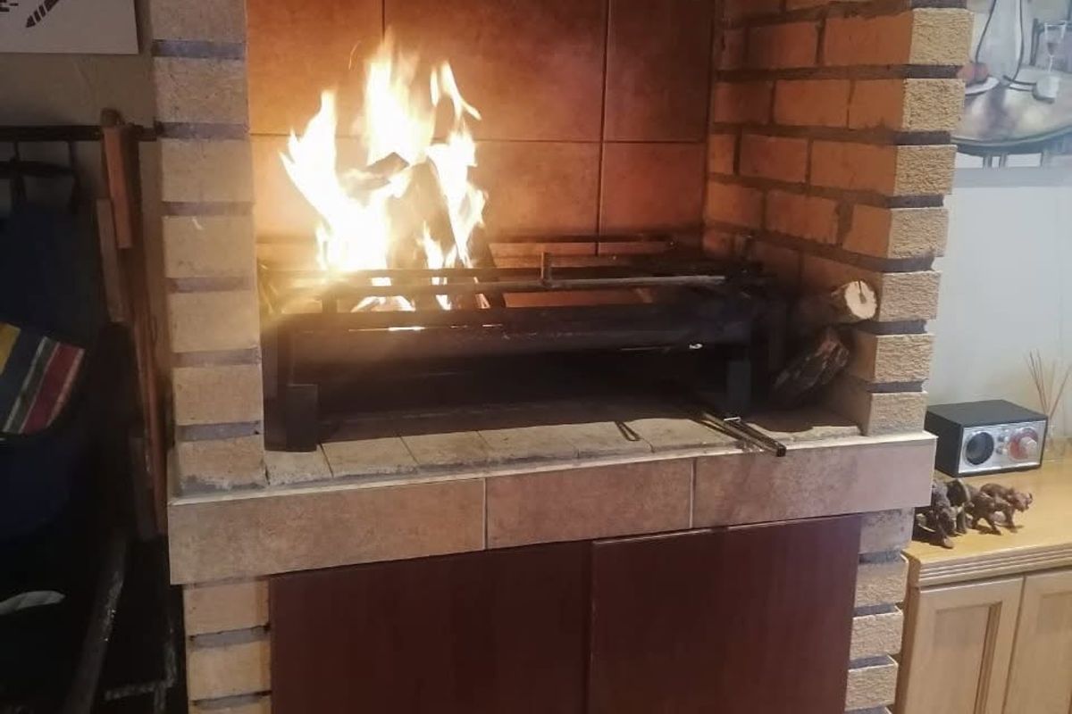 A traditional indoor brick fireplace and built-in braai area featuring a tiled hearth and integrated lower storage cabinetry.