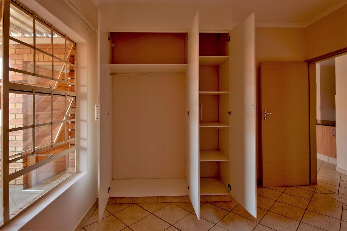A bright, empty bedroom featuring tiled flooring, a built-in wardrobe with shelving, and a window with security bars.
