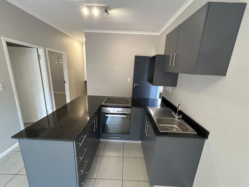 Modern kitchen featuring grey cabinetry, granite countertops, built-in oven, electric hob, and stainless steel sink with tiled flooring.