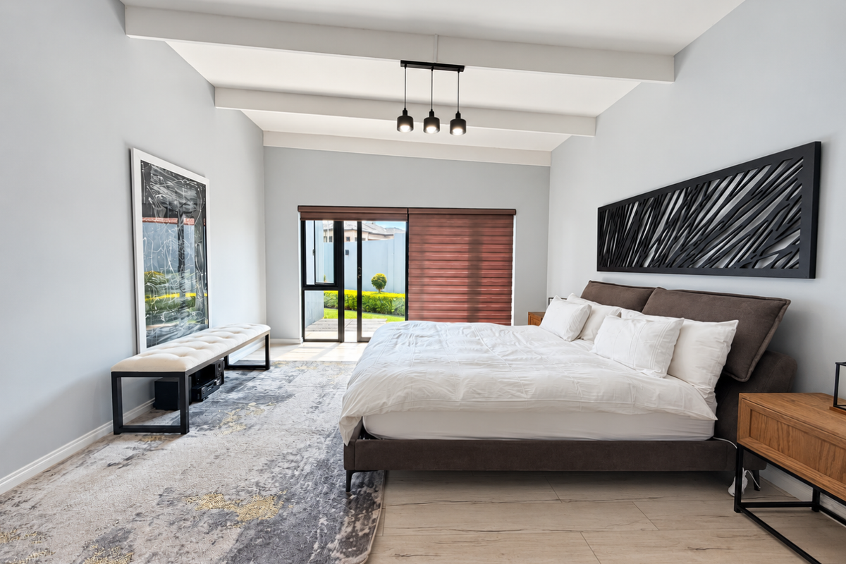 Spacious bedroom featuring exposed ceiling beams, wood-look tile flooring, and a sliding glass door providing direct access to the outdoor area.