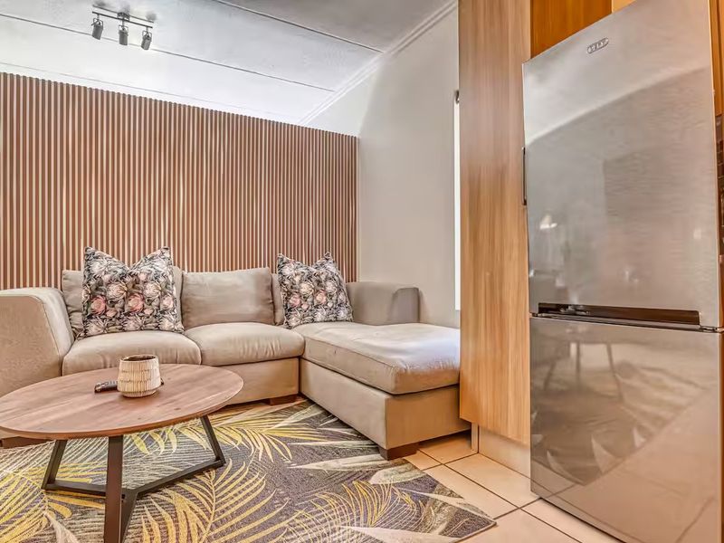Modern open-plan living area featuring stylish slatted wood wall paneling, neutral tiled flooring, and contemporary track lighting.