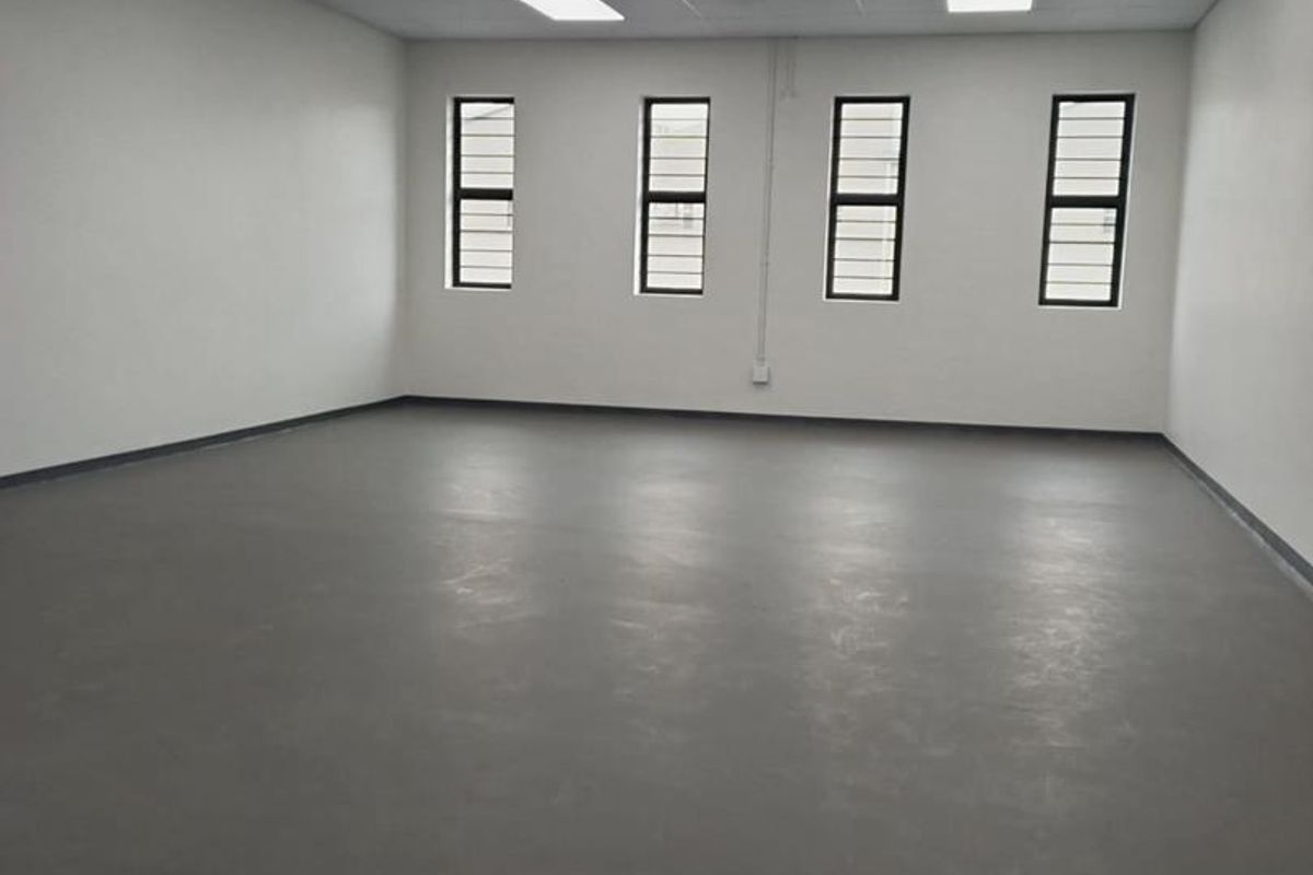 A clean, vacant industrial office space featuring neutral walls, durable flooring, recessed ceiling lighting, and windows fitted with security bars.