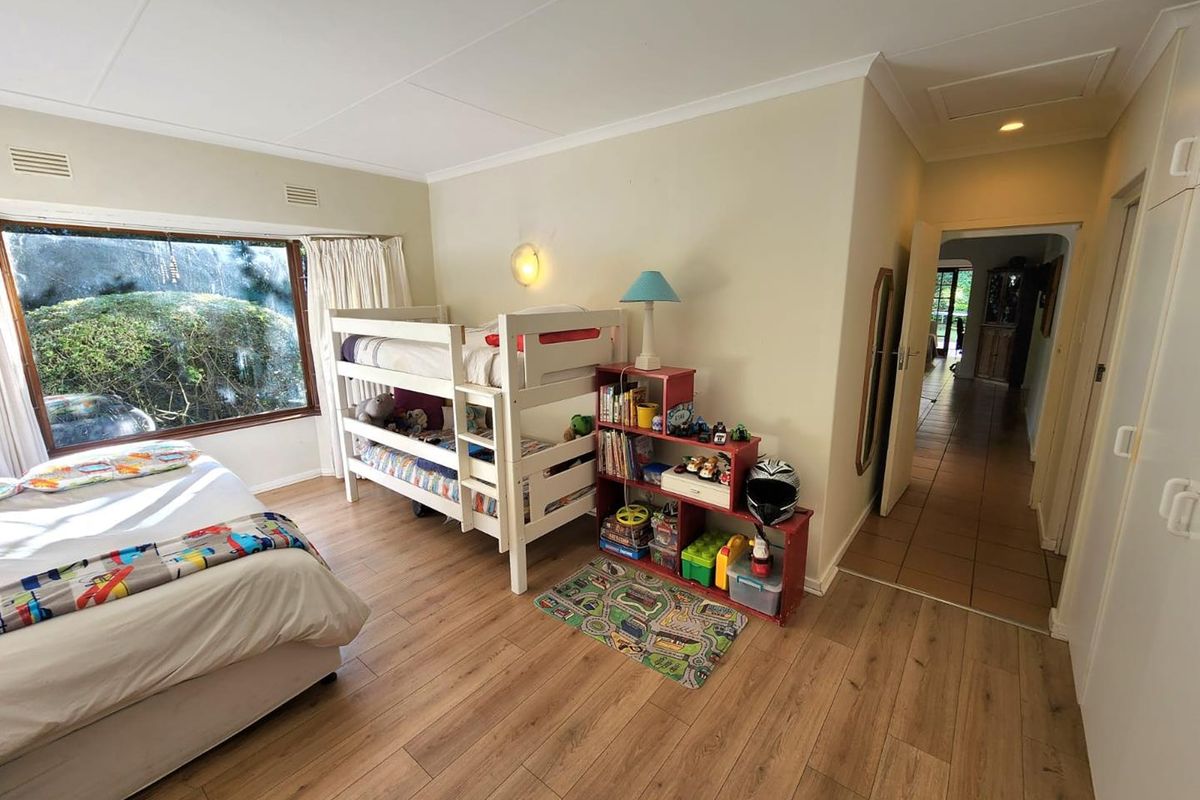 A spacious bedroom featuring wood-look laminate flooring, large windows providing natural light, and built-in cupboard storage.