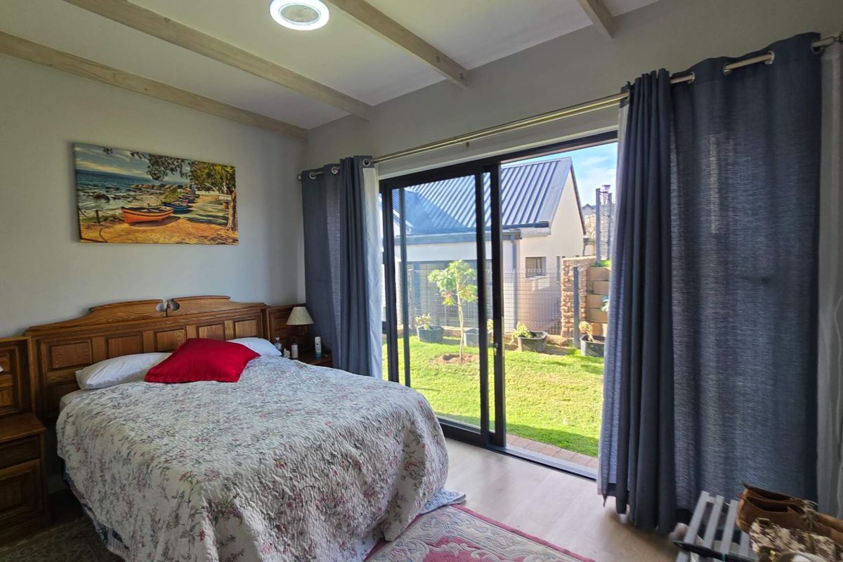 A bright bedroom featuring laminate flooring, exposed ceiling beams, and a large sliding glass door providing direct access to the rear garden.