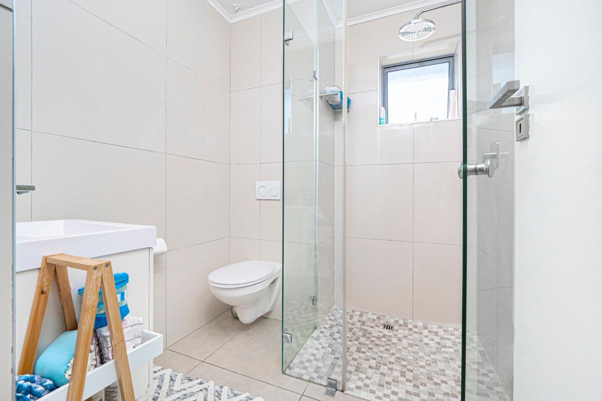 Modern bathroom featuring a glass-enclosed walk-in shower, wall-mounted toilet, and a sleek vanity unit with neutral floor-to-ceiling tiling.